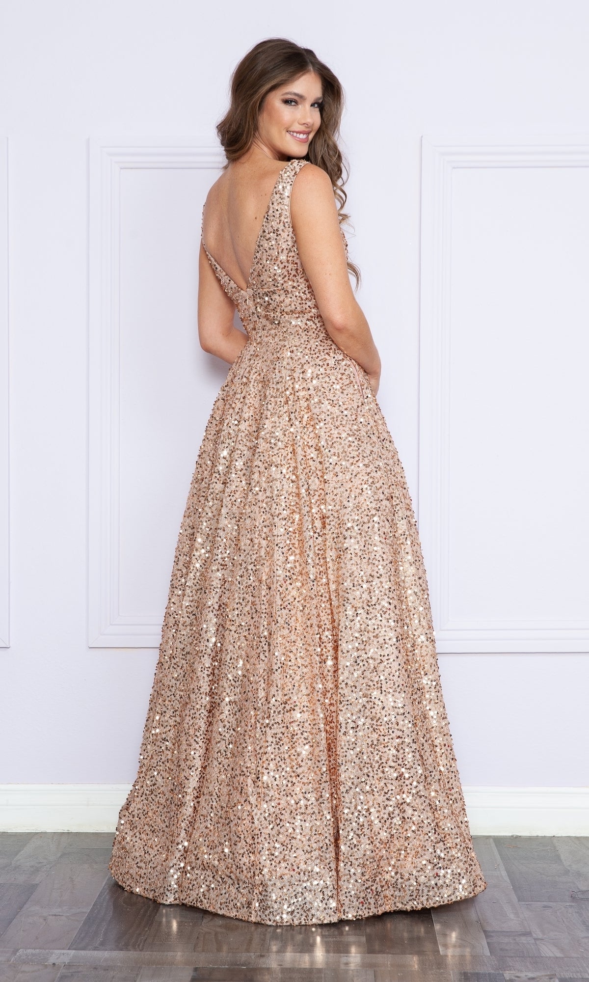 A woman in a floor-length, sleeveless Long Black Sequin A-Line Prom Dress 9168 stands with her back to the camera, looking over her shoulder and smiling.